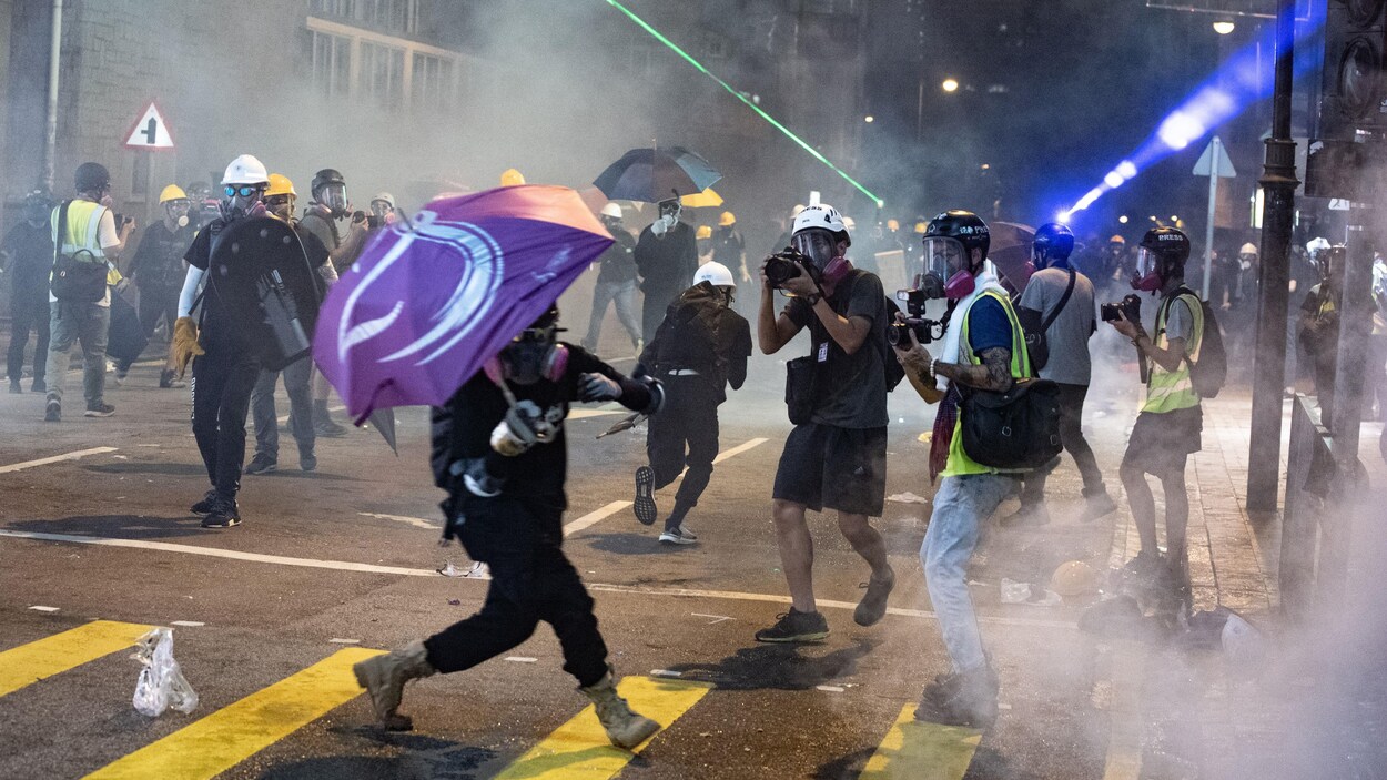 Des manifestants avec des masques à gaz s'éparpillent sous les jets de bombes lacrymogènes.