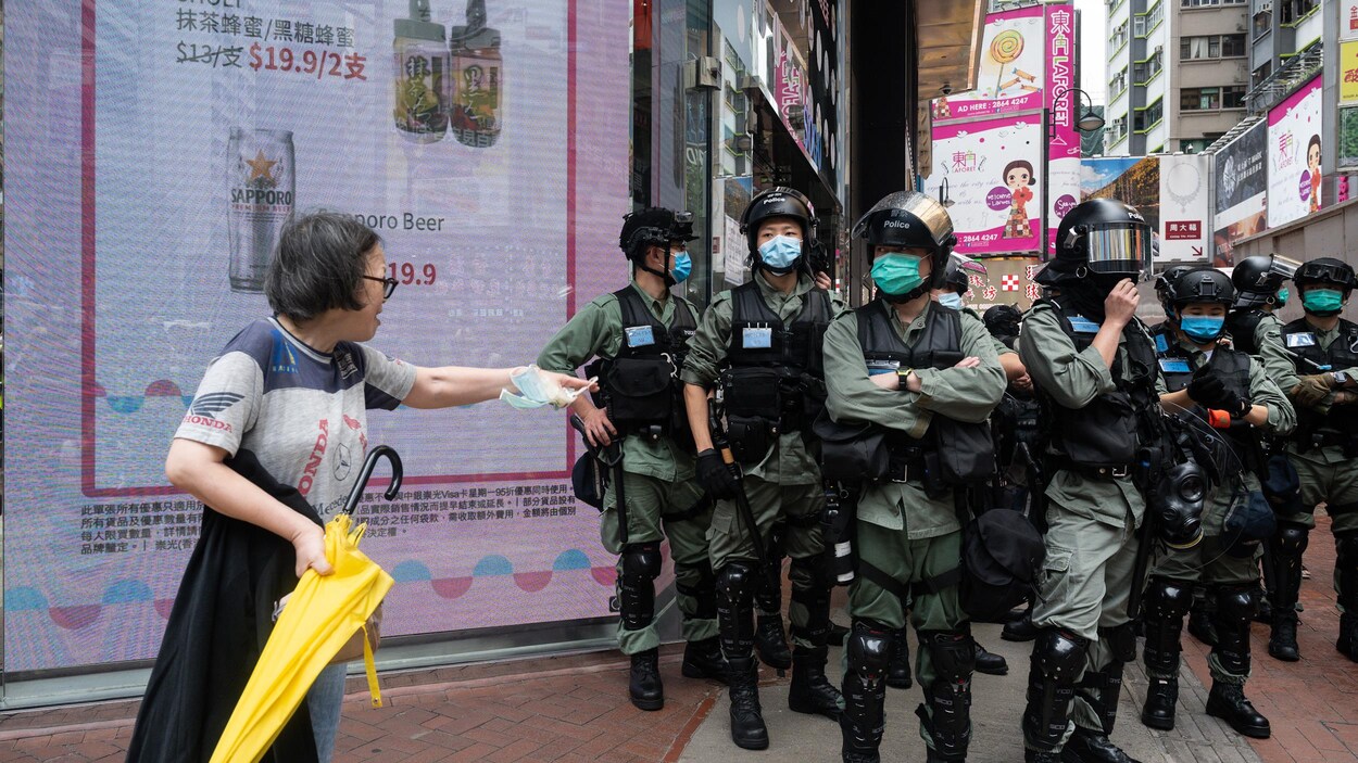 Une femme interpelle des policiers en tenue antiémeute dans une rue de Hong Kong.