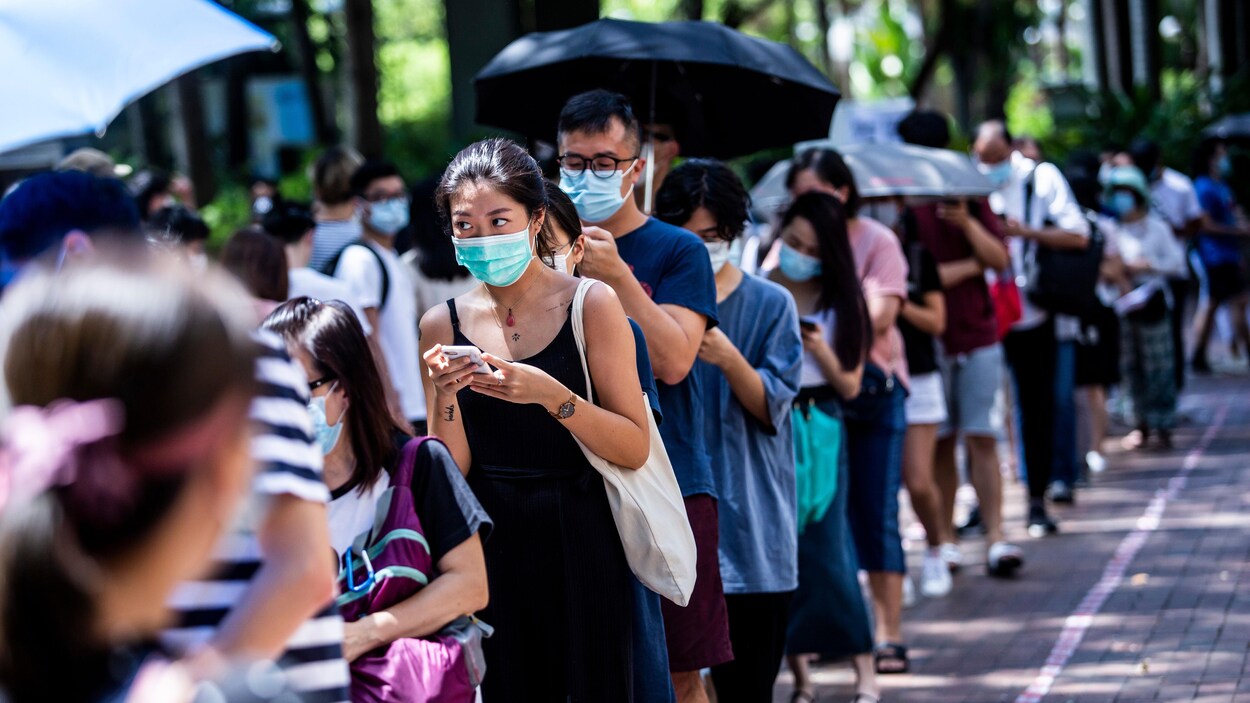 Une femme (centre) utilise son téléphone en attendant de voter lors des élections primaires à Hong Kong.
