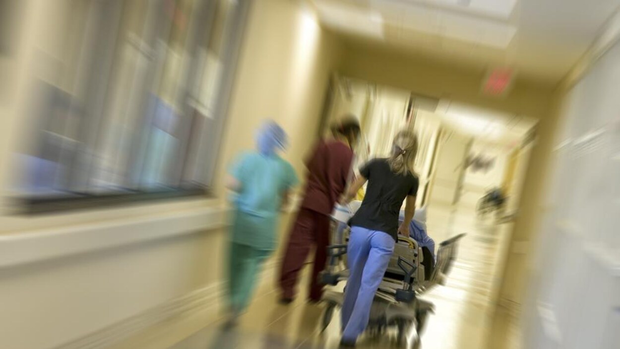 Une infirmière fait rouler un lit dans un couloir d'hôpital.