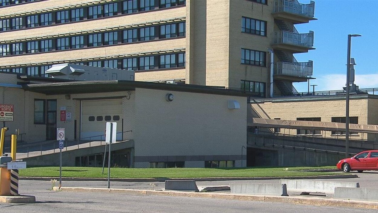 Une petite voiture rouge se trouve dans le stationnement d'un hôpital.