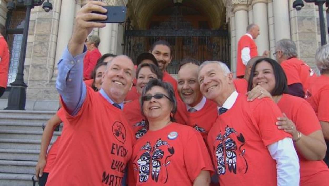 Le premier ministre de la Colombie-Britannique, John Horgan, entouré de membres de son Cabinet et de Phyllis Webstad, qui a proposé le port du chandail orange, lors de la prise d'un égoportrait sur les marches de l'assemblée législative à Victoria. Le premier ministre de la Colombie-Britannique, John Horgan, entouré de membres de son Cabinet et de Phyllis Webstad, qui a proposé le port du chandail orange, lors de la prise d'un égoportrait sur les marches de l'assemblée législative à Victoria.