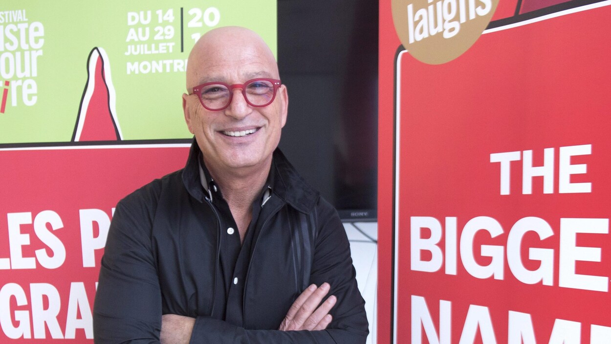 L'humoriste Howie Mandel, souriant prend la pose, debout, les bras croisés, devant des affiches promotionnelles de Juste pour rire. L'humoriste Howie Mandel, souriant prend la pose, debout, les bras croisés, devant des affiches promotionnelles de Juste pour rire.