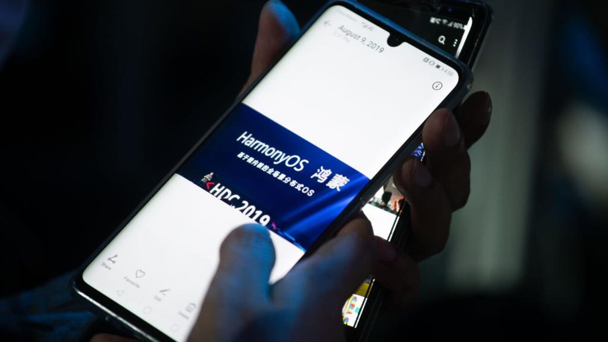 HarmonyOS est écrit sur l'écran d'un téléphone intelligent tenu par une main.