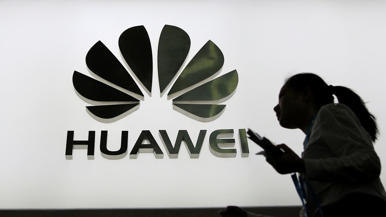 Des personnes marchent devant un panneau lumineux montrant le logo de Huawei.