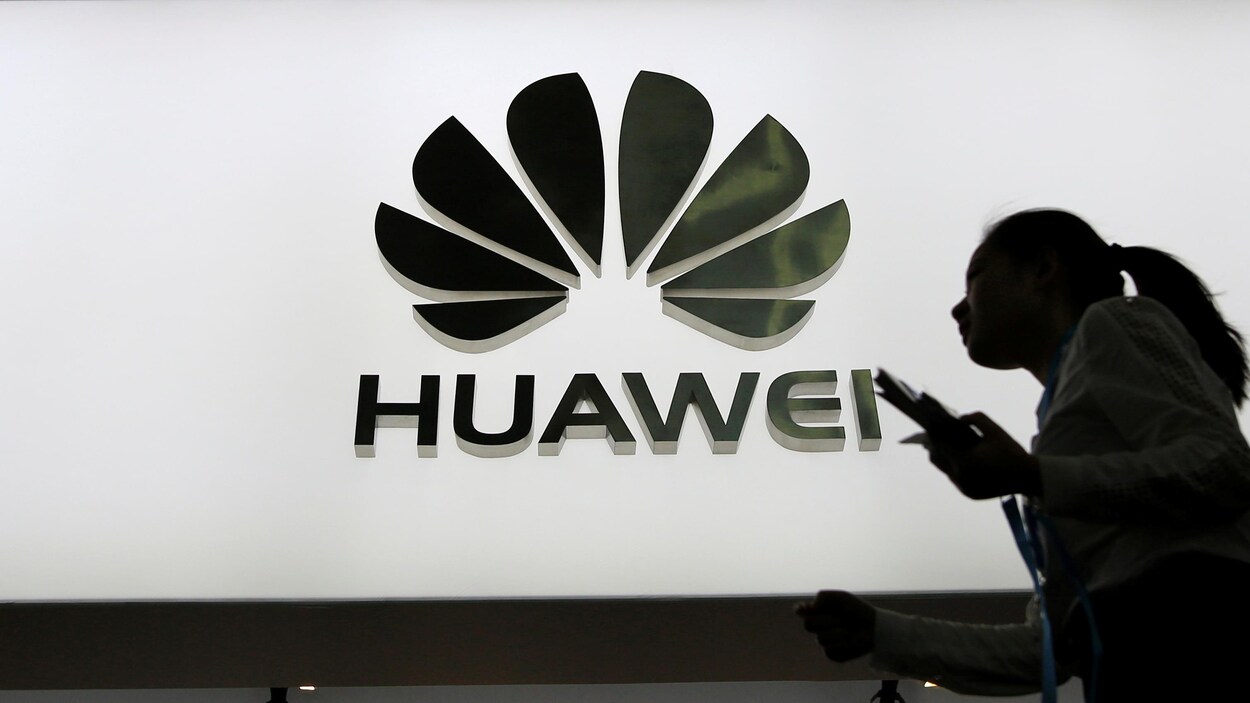 Des personnes marchent devant un panneau lumineux montrant le logo de Huawei.