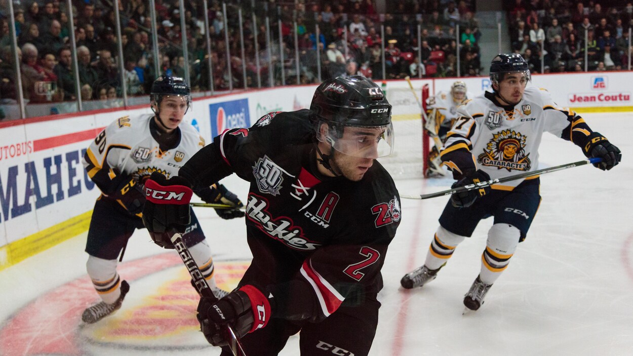 Peter Abbandonato avance sur la glace devant deux joueurs des Cataractes. Plusieurs partisans se trouvent aussi dans l'aréna Iamgold de Rouyn-Noranda.