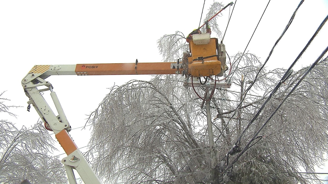 Un homme au sommet d'une grue répare des fils électriques endommagés par le verglas.