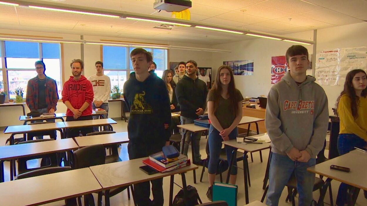 Des élèves debout, les mains croisées, écoutant l'hymne national canadien.