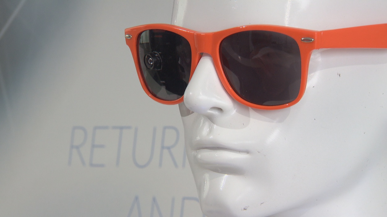 Une tête de mannequin porte une lunette orange sur laquelle on voit une petite caméra.