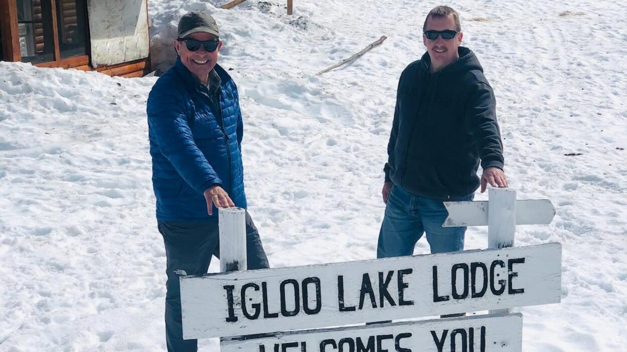 Deux employés devant une pancarte qui annonce le camp de pêche.