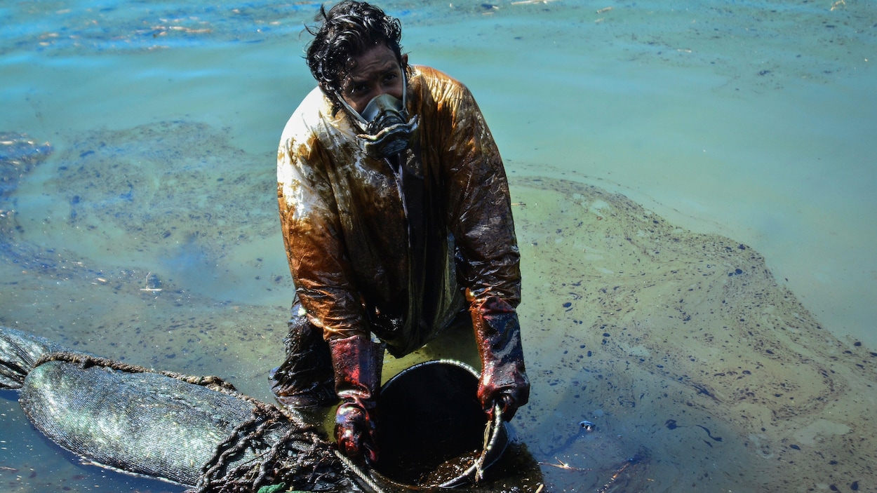 Un homme récupère du pétrole qui s’est déversé dans la mer à l’aide d’un genre de tamis.