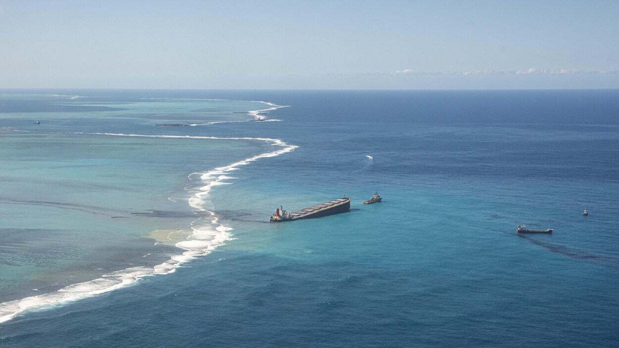 Le pétrolier en mer est incliné d'un côté. Deux bateaux plus petits sont à proximité.