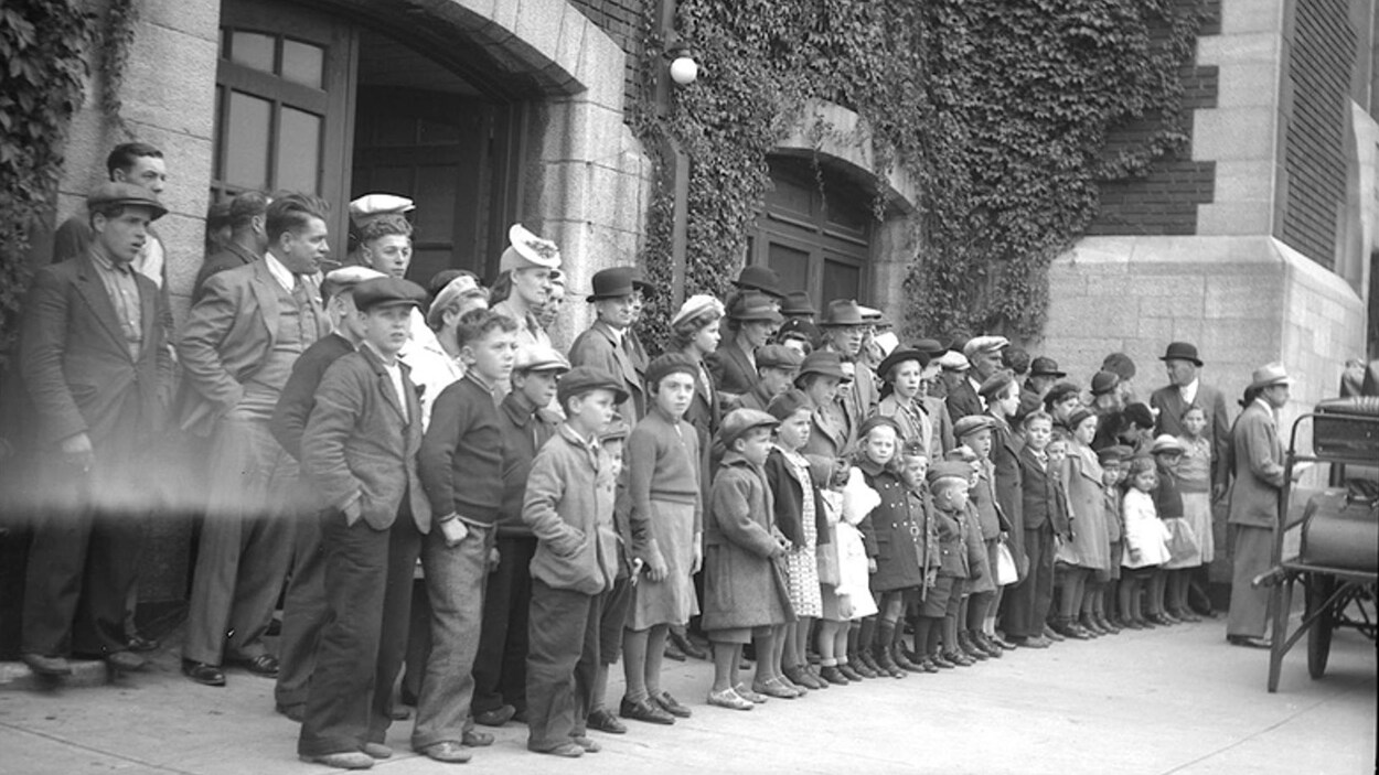 Photo noir et blanc du premier groupe de Madelinots qui prennent la direction de l'Abitibi en 1941. Ils sont réunis à la gare de Québec, les hommes et les femmes derrière, les enfants devant. Photo noir et blanc du premier groupe de Madelinots qui prennent la direction de l'Abitibi en 1941. Ils sont réunis à la gare de Québec, les hommes et les femmes derrière, les enfants devant.