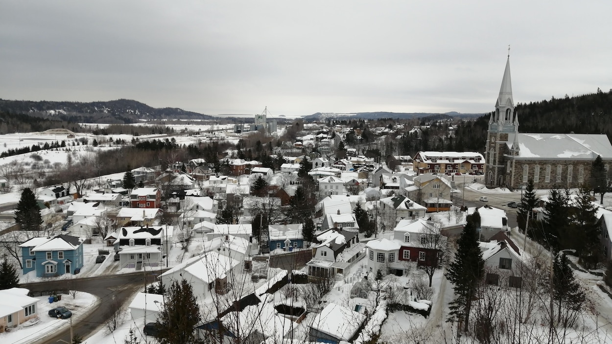 Vue en plongée sur des maisons aux toits enneigés et une église de pierres.