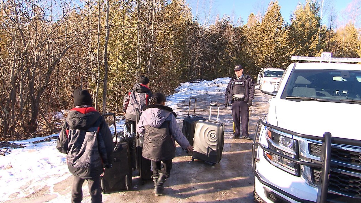 Des enfants, dont la famille a tenté d'entrer illégalement au Canada, marchent dans la neige en direction d'un policier. Des enfants, dont la famille a tenté d'entrer illégalement au Canada, marchent dans la neige en direction d'un policier.