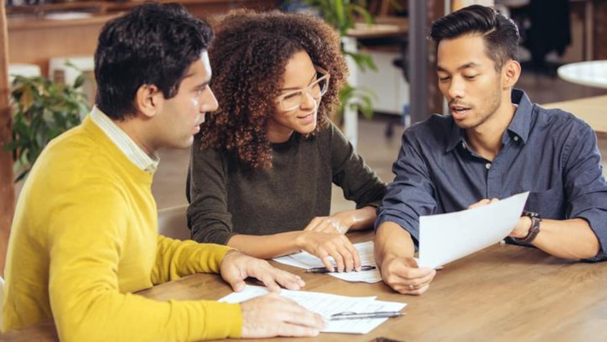 Trois personnes issues des minorités visibles autour d'une table et devant des documents. Trois personnes issues des minorités visibles autour d'une table et devant des documents.