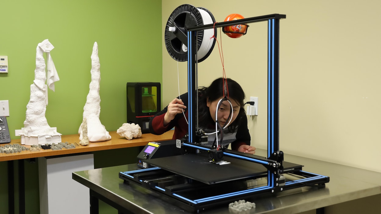Une personne ajuste l'imprimante 3D en cours d'impression.