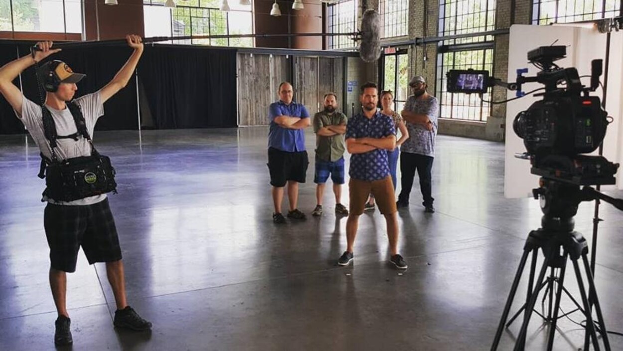 un groupe dans une salle de studio aéré devant une caméra avec un preneur de son qui tend sa perche.