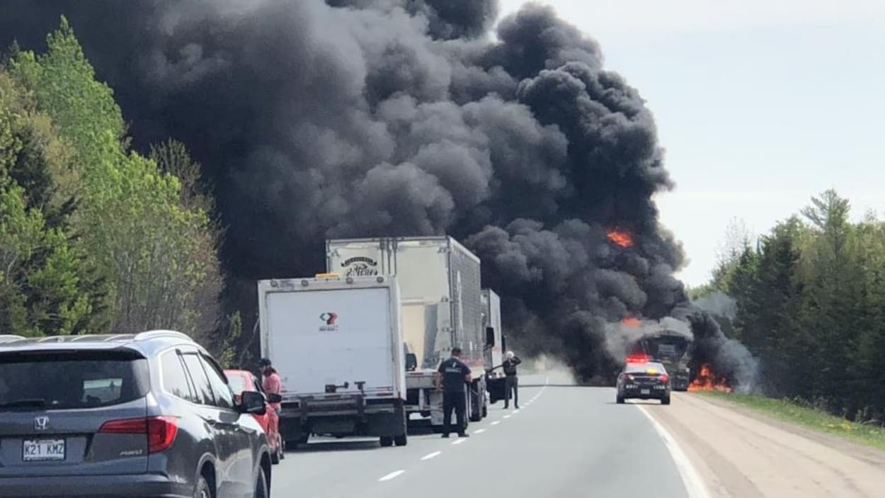 Un véhicule en feu sur l'autoroute dégage beaucoup de fumée noire.
