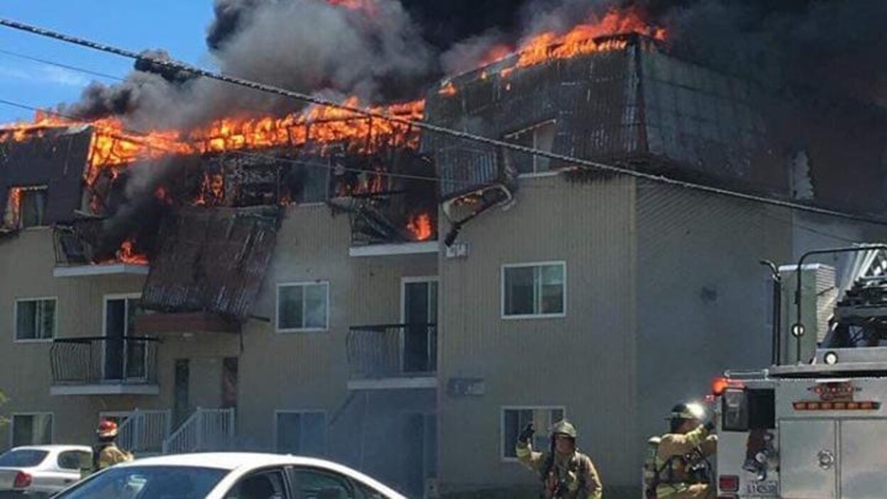 Un périmètre de sécurité et des pompiers devant un immeuble en feu.