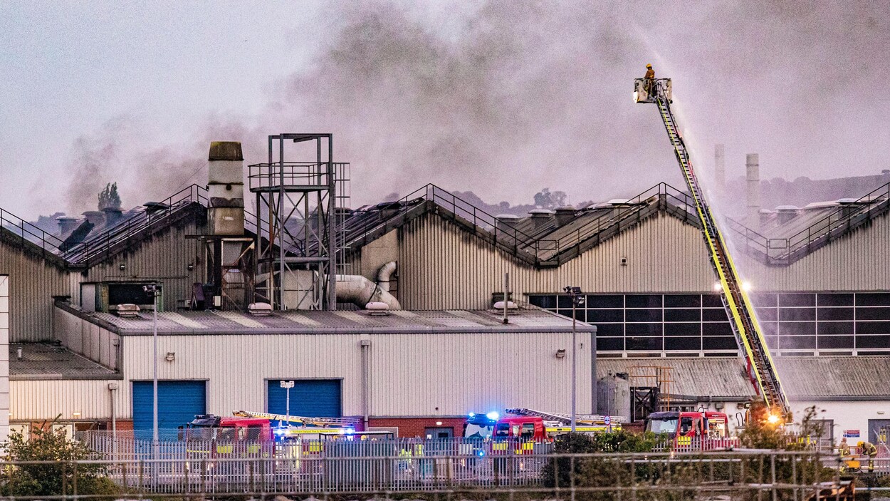 Un pompier au bout de la grande échelle arrose l'incendie dans l'usine.