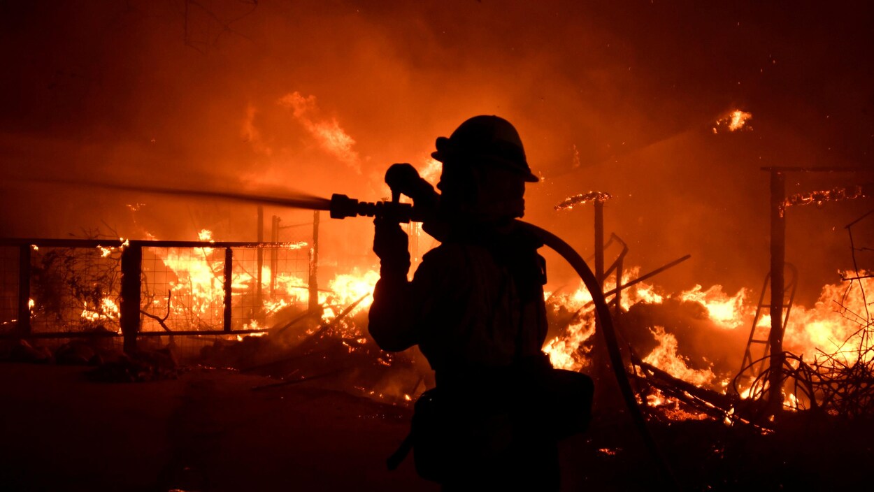 Un pompier lutte contre les flammes à l'aide d'un boyau d'incendie.