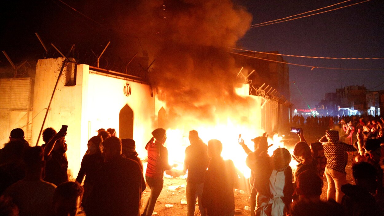 Des manifestants devant un édifice en flammes.