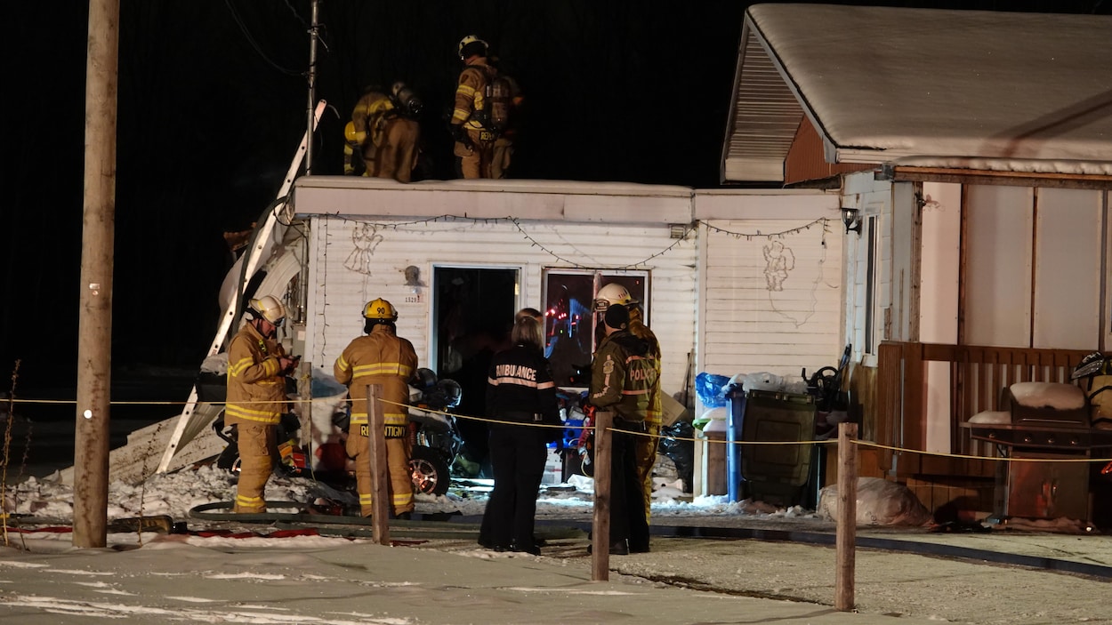 Cinq pompiers, une ambulancière et un policier s'affaire dans le bungalow adjascent une maison.