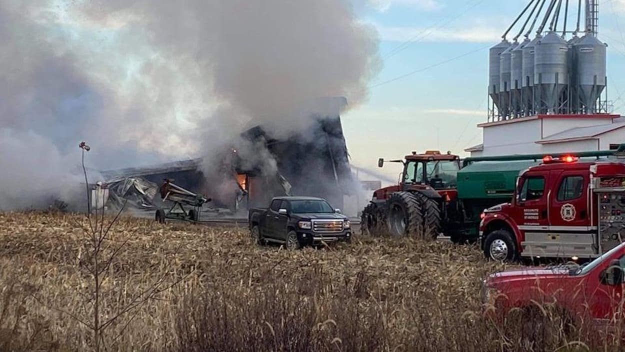 Des pompiers sont présents aux abords d'un garage agricole en flamme.