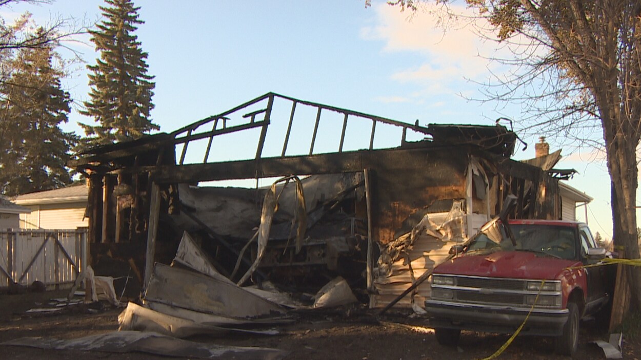 Les ruines d'un garage à la suite d'un incendie. La voiture stationnée contre le bâtiment est aussi endommagée.