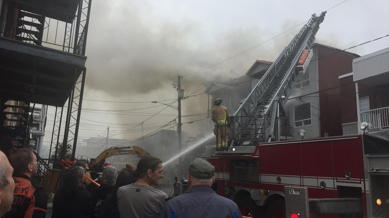 Des passants regardent des pompiers combattre un incendie.