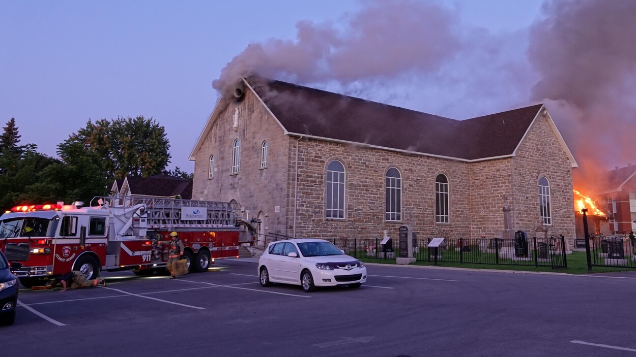 Des flammes s'élèvent d'une église, un camion de pompiers arrive sur les lieux.
