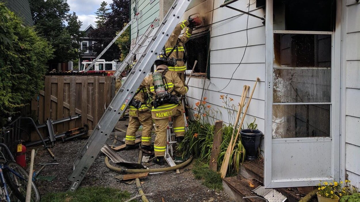 Trois pompiers près d'une maison incendiée.