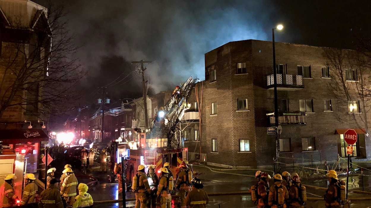 Des groupes de pompiers se consultent pendant que d'autres interviennent directement dans le bâtiment pour éteindre l'incendie.