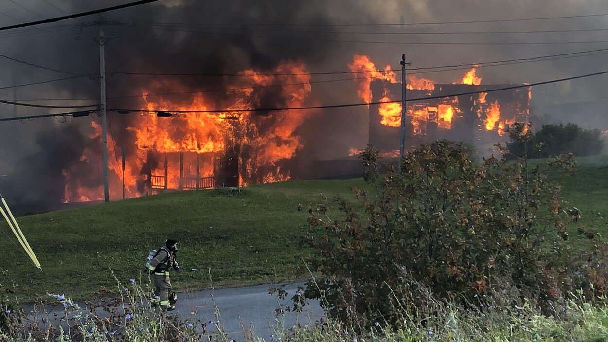 Deux maisons sont en proie aux flammes pendant qu'un pompier travaille sur le terrain.