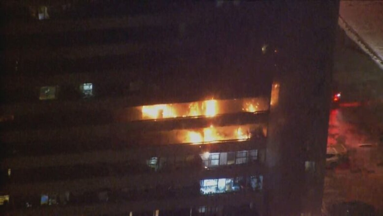 Un immeuble de logements avec des flammes sur plusieurs étages, la nuit.