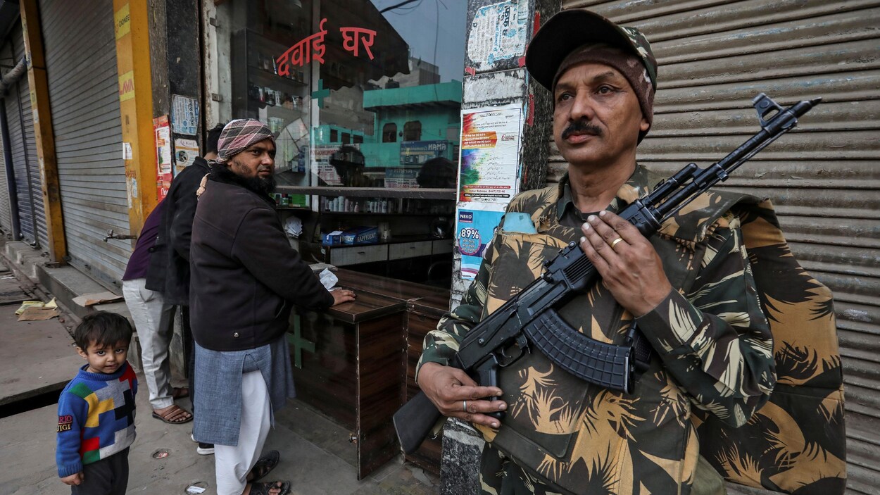 Un homme armé se tient devant une boutique fermée.
