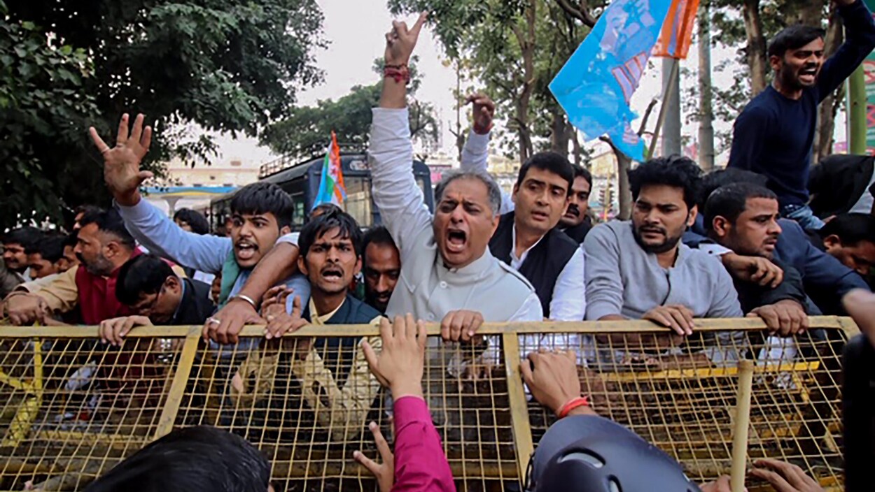 Des hommes crient derrière une barrière de métal en Inde.