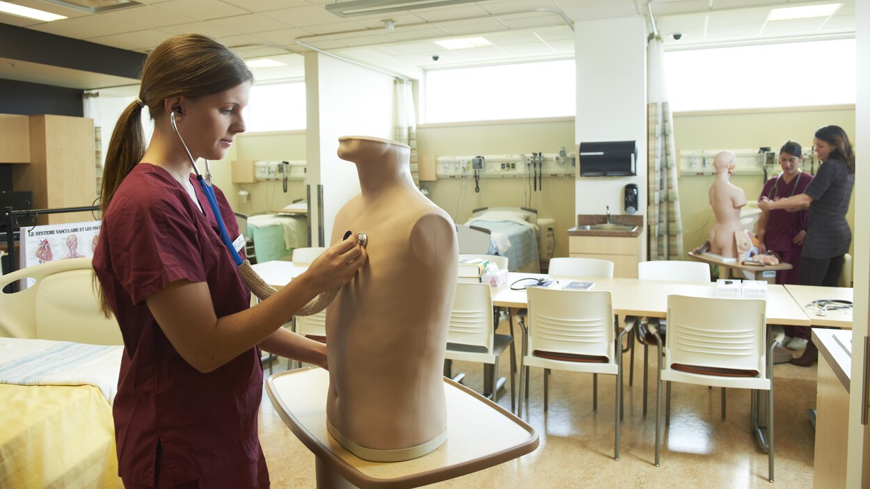 Une jeune femme tâte un mannequin avec un stéthoscope.