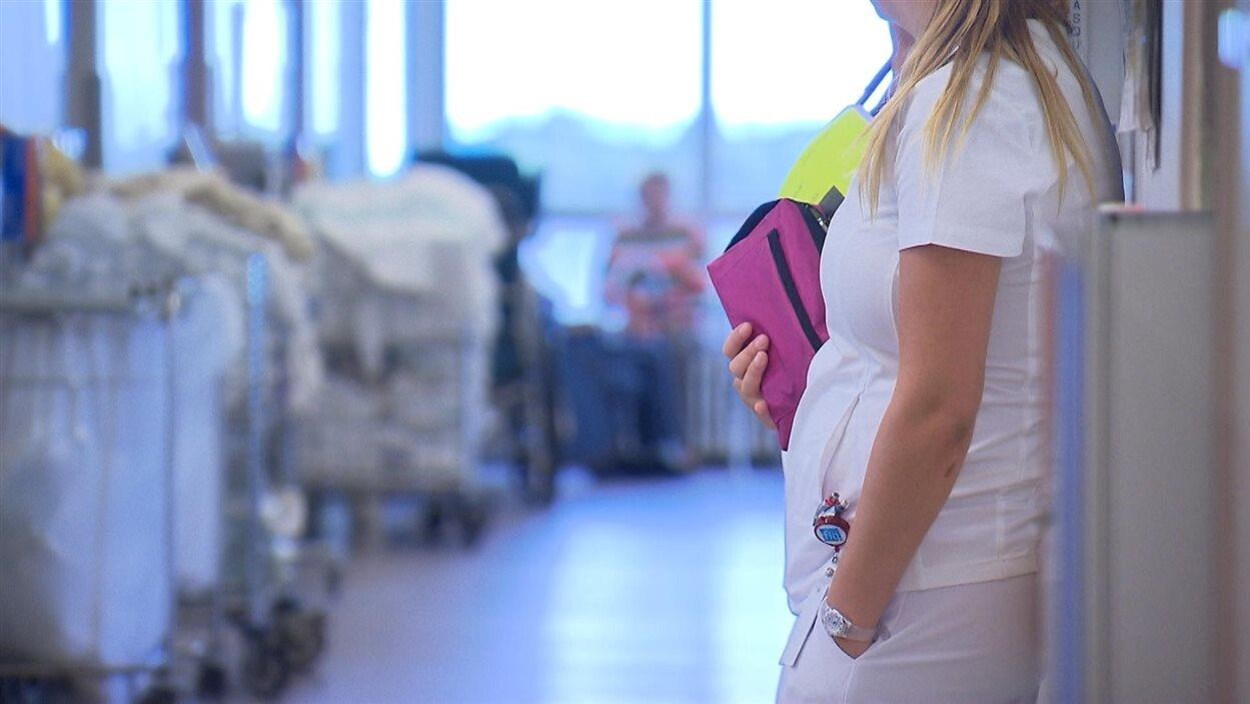 Une infirmière qui tient un étui est debout dans un corridor d'hôpital.