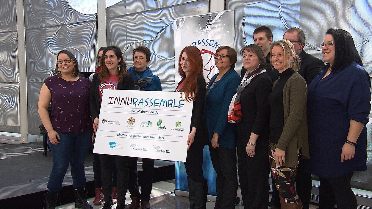 Plusieurs personnes sourient à la caméra avec une affiche d'InnuRassemble