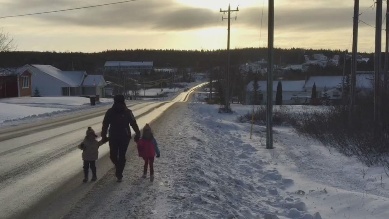 Une femme et deux enfants marchent le long d'une route dans un village en hiver.