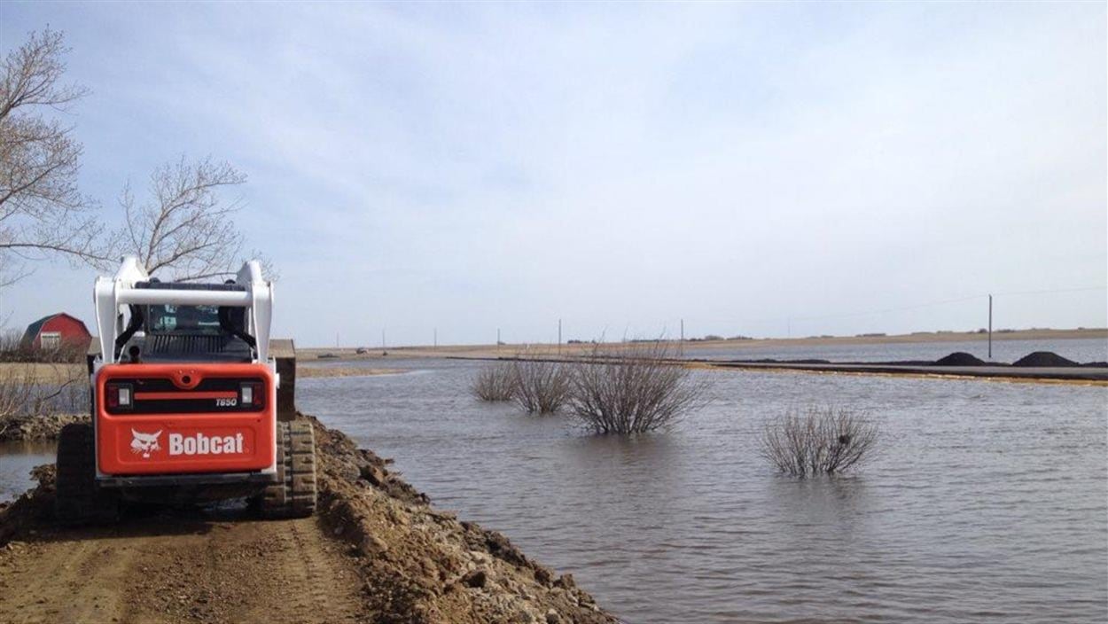 Une petite excavatrice avance sur un chemin de terre surélevé dans un champ inondé. Une petite excavatrice avance sur un chemin de terre surélevé dans un champ inondé.