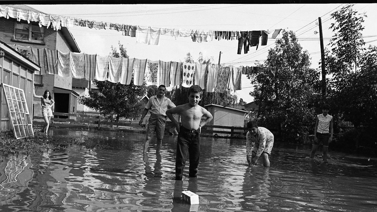 Une photo en noir et blanc où l'on voit une famille, les deux pieds dans l'eau.