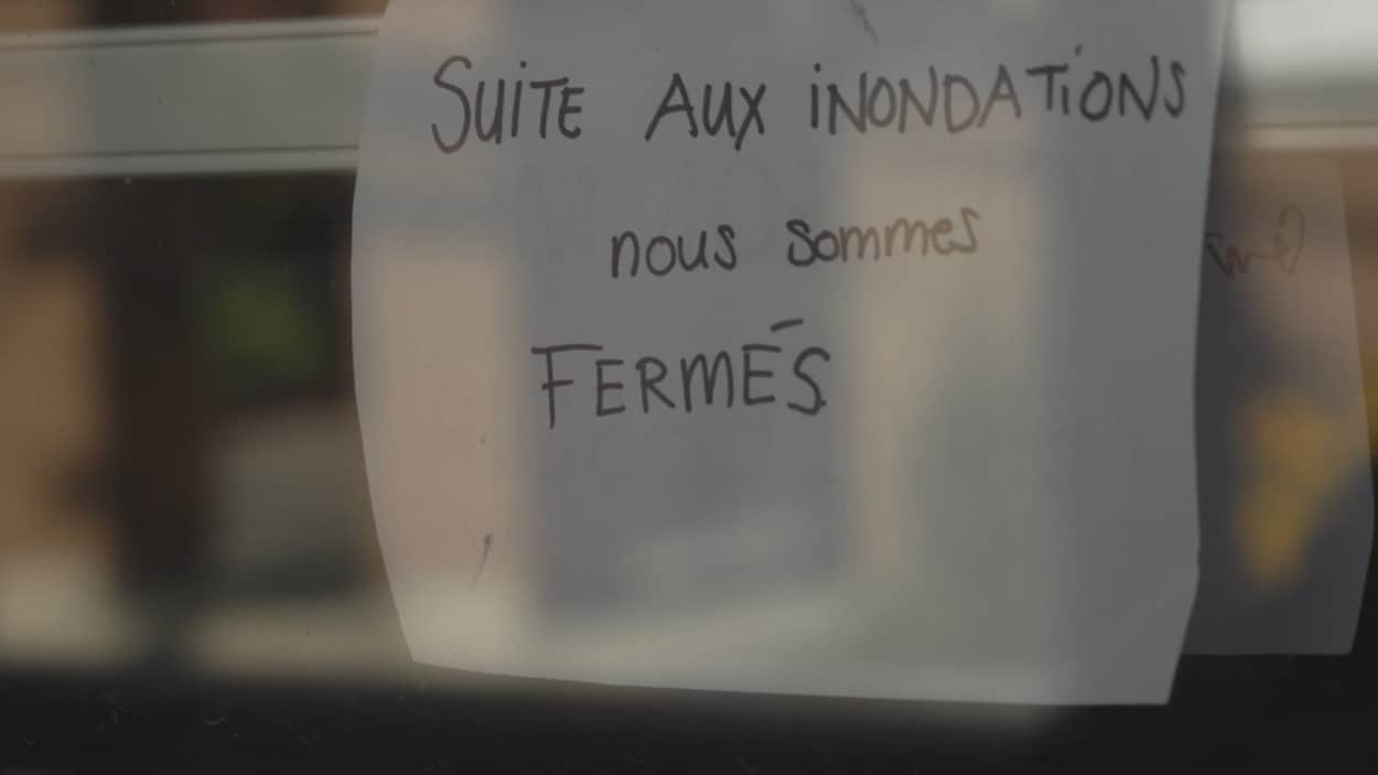 Une affiche accrochée à une porte indique que le commerce est fermé à la suite des inondations.