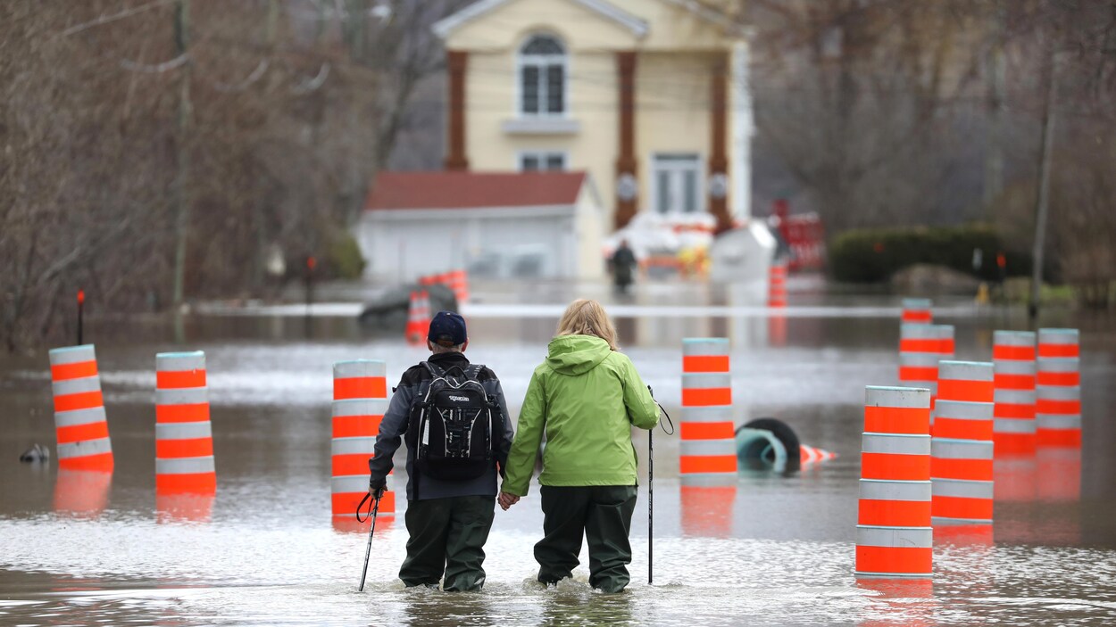 Un homme et une femme se tiennent la main en marchant dans un quartier résidentiel inondé de Gatineau.