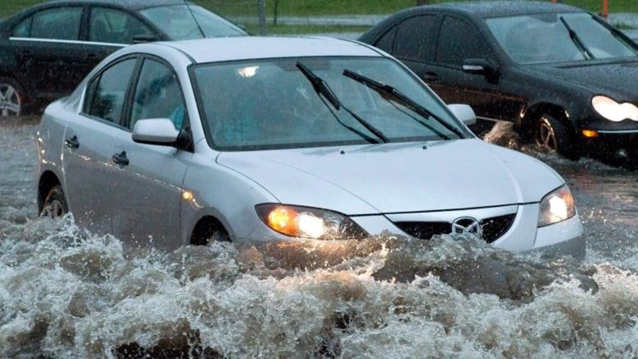Image d'une voiture prise par les eaux sur une route.