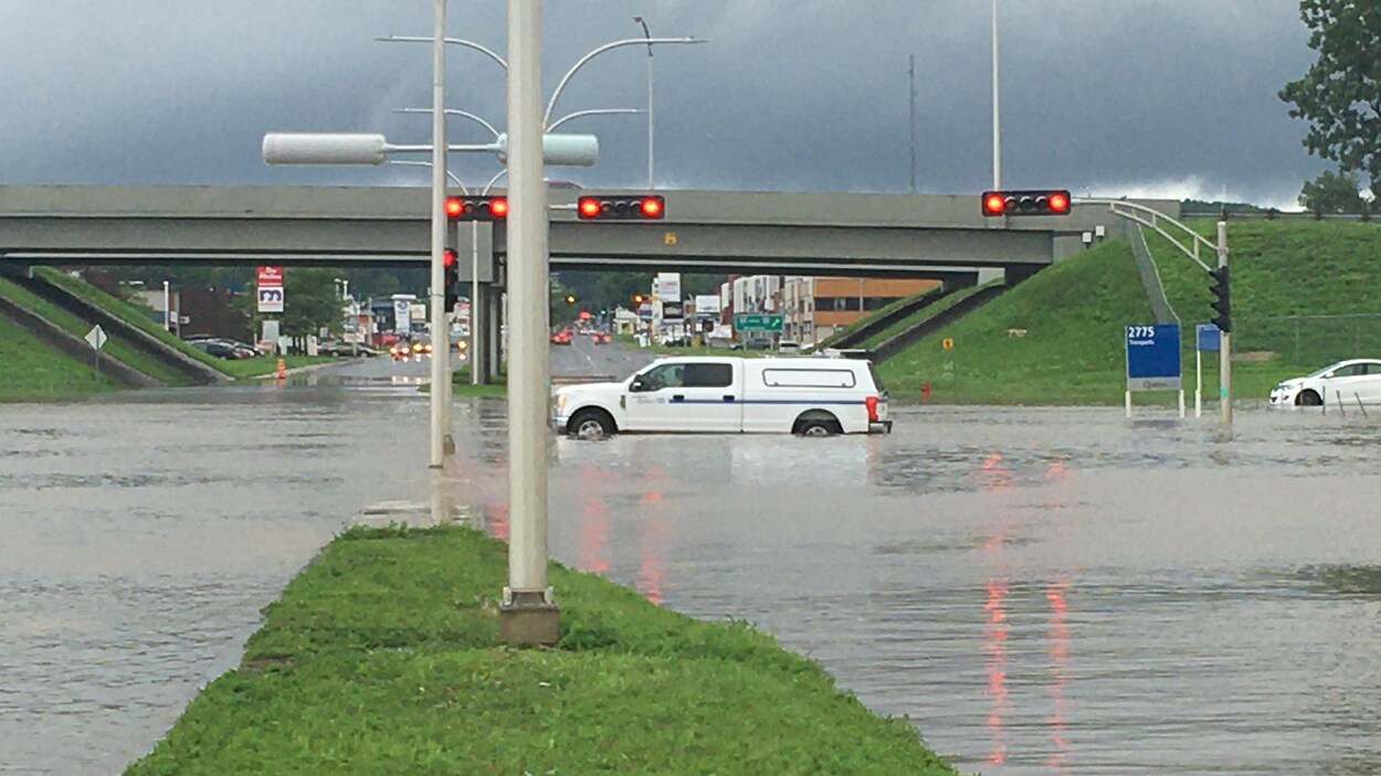 Une voiture traverse la rue. Ses roues sont submergées d'eau. C'est un soin inondé.