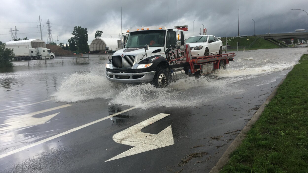 Une remorqueuse transporte une voiture à l'arrière. De l'eau sort des roues, en roulant.